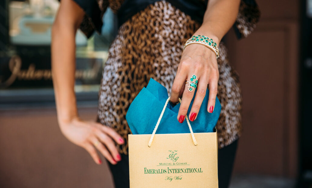 Photo of a female with an emerald ring and bracelet holding an emeralds international shopping bag.