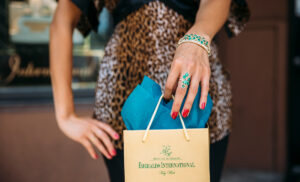 Photo of a female with an emerald ring and bracelet holding an emeralds international shopping bag.