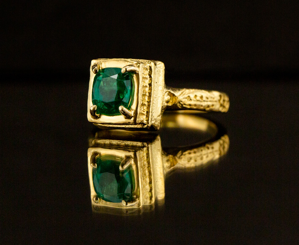 Mudejar style ring with Colombian emerald on a reflective material with black background.