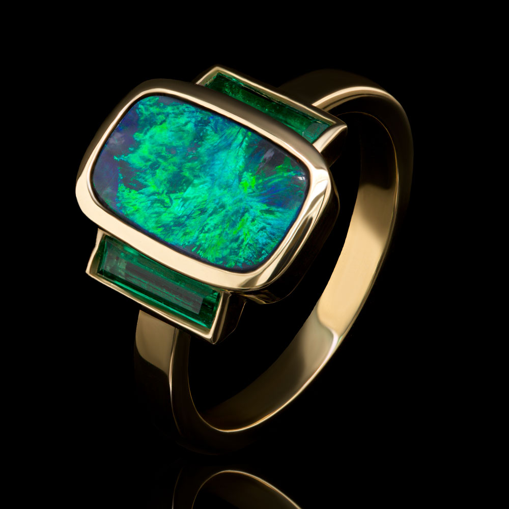 Opal & Emerald Three Stone Ring on a black background.